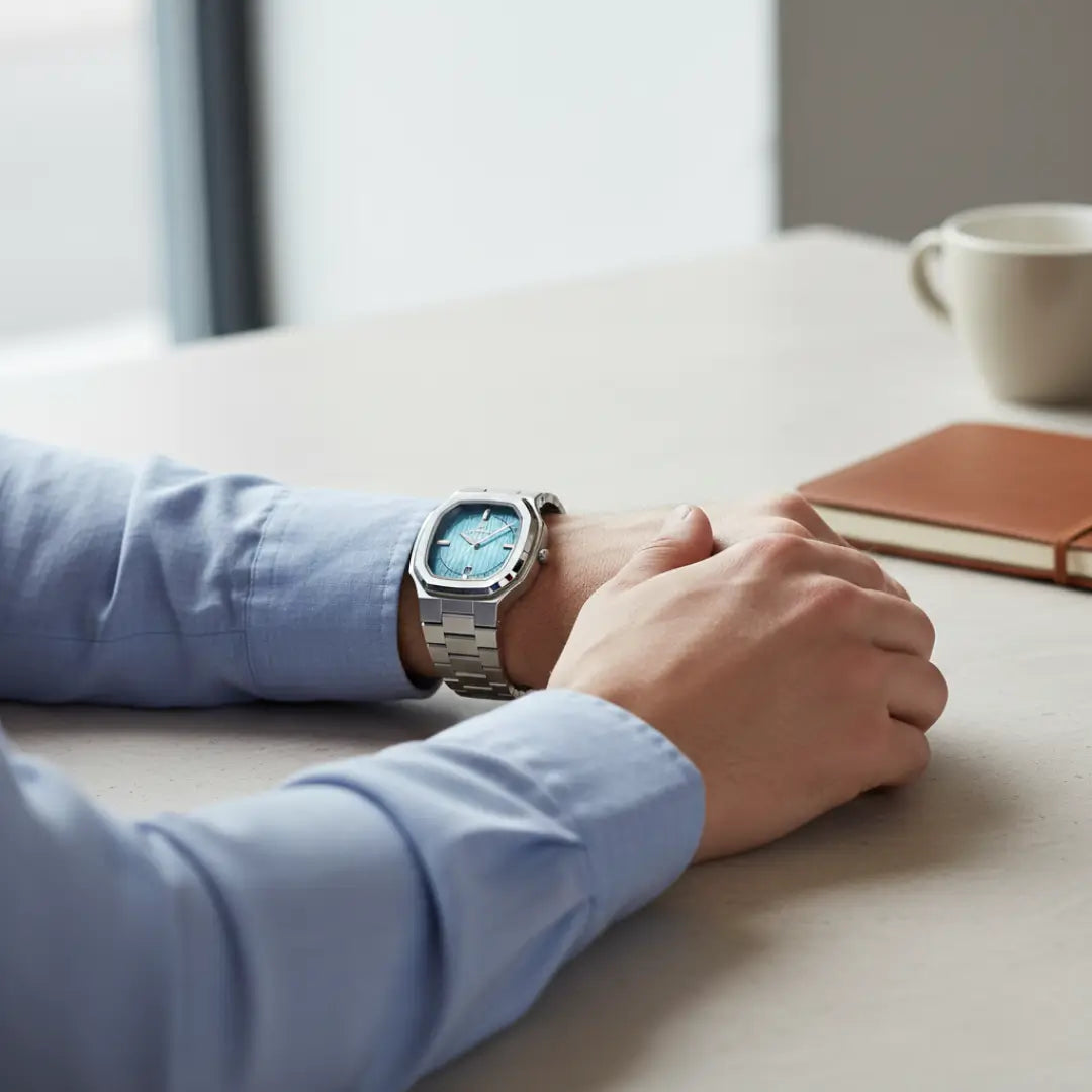 Relógio social masculino Signature prata com caixa octogonal de 38mm no pulso, em ambiente de café e descanso.