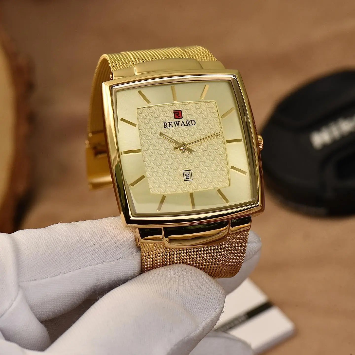Close no mostrador e nos detalhes dourados do relógio masculino Reward VIP Monaco Date, segurado por mão com luva

