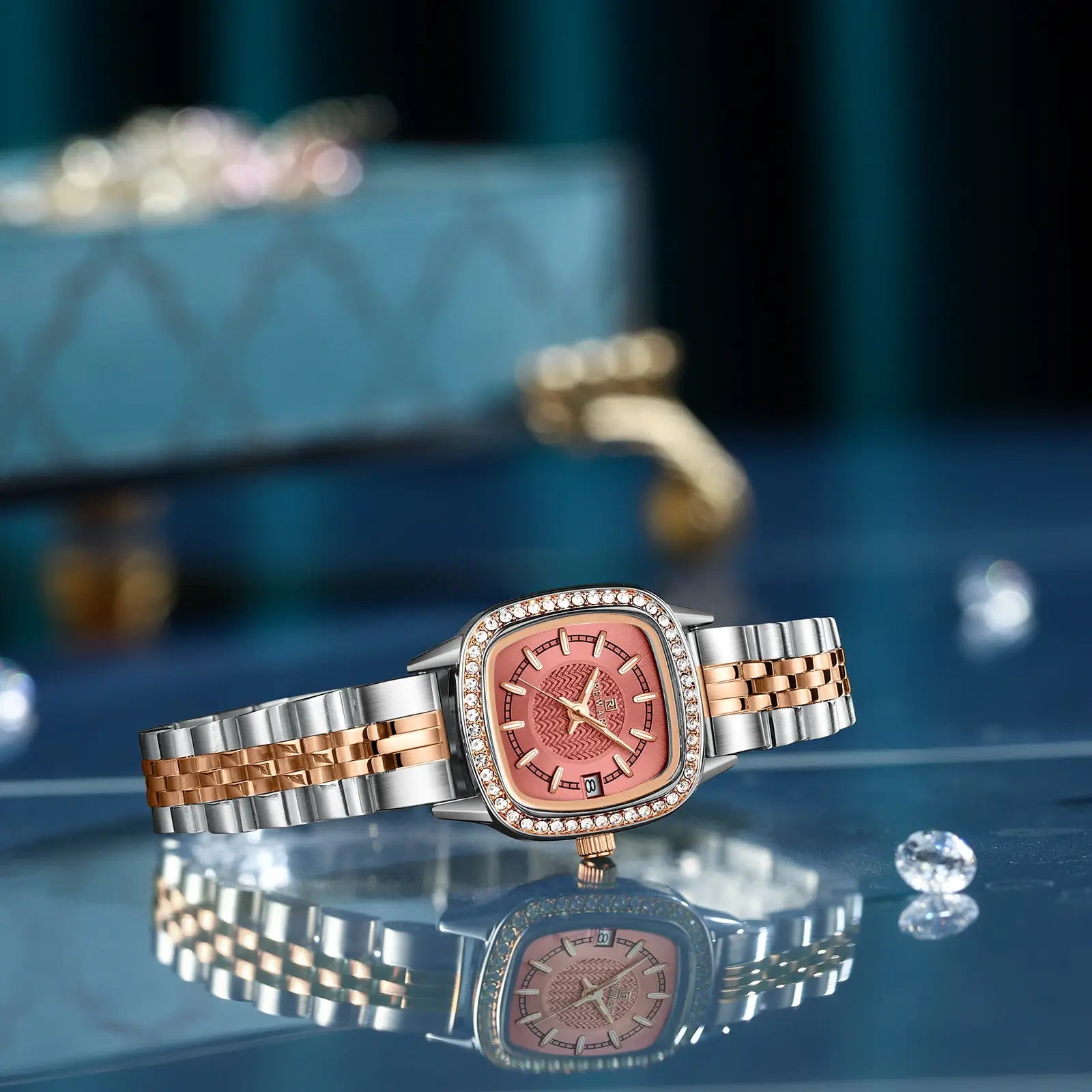 Relógio quadrado feminino pequeno prata com mostrador rosa e pulseira em aço visto com foco no mostrador e bisel com pedras brilhantes