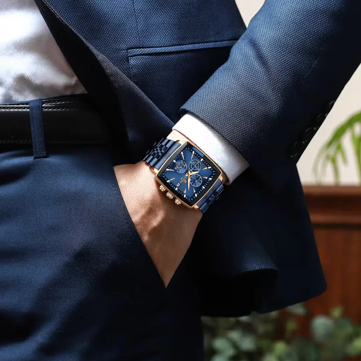 Homem elegante de terno usando um relógio masculino sofisticado e social com formato quadrado com cores vibrantes no tom azul marinho e dourado 